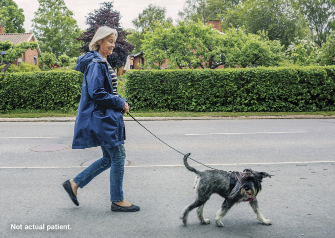 Woman in blue jacket walking her dog on a street. Not actual patient.